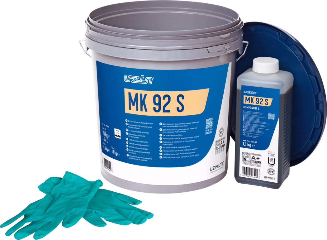 UZIN_Dummy_MK 92 S-10kg_2024-09 Studiijska fotografija kompleta za parketni ljepilo: veliki sivi plastični kanta s upečatljivom plavom etiketom 'MK 92 S', desno manja pravokutna boca označena 'MK 92 S Component B' s bijelim čepom, a tamno plavi poklopac naslonjen je u pozadini. U prvom planu je par tirkiznih jednokratnih rukavica. Predmeti su raspoređeni na bijeloj pozadini s ujednačenim osvjetljenjem, naglašavajući detalje ambalaže i informacije o proizvodu za postavljanje podova.